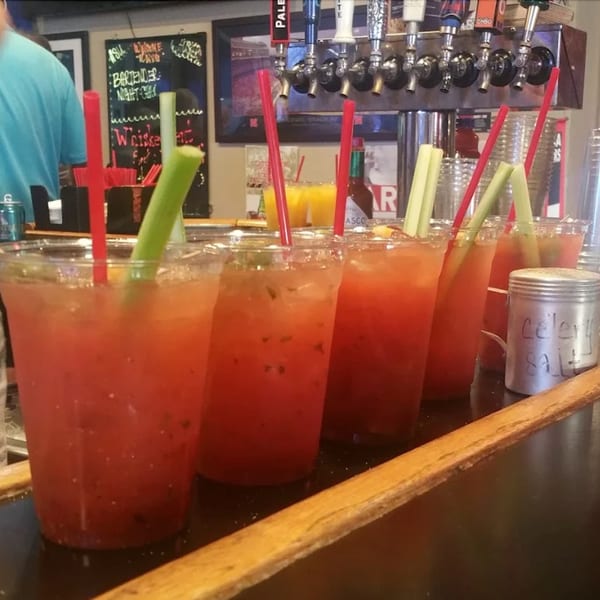 Row of Moon Valley Grill & Patio Bloody Marys with celery and red straws on a bar.