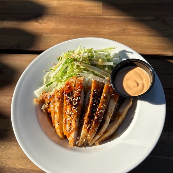 Teriyaki chicken with sesame seeds, a side salad, and dipping sauce on a white plate.