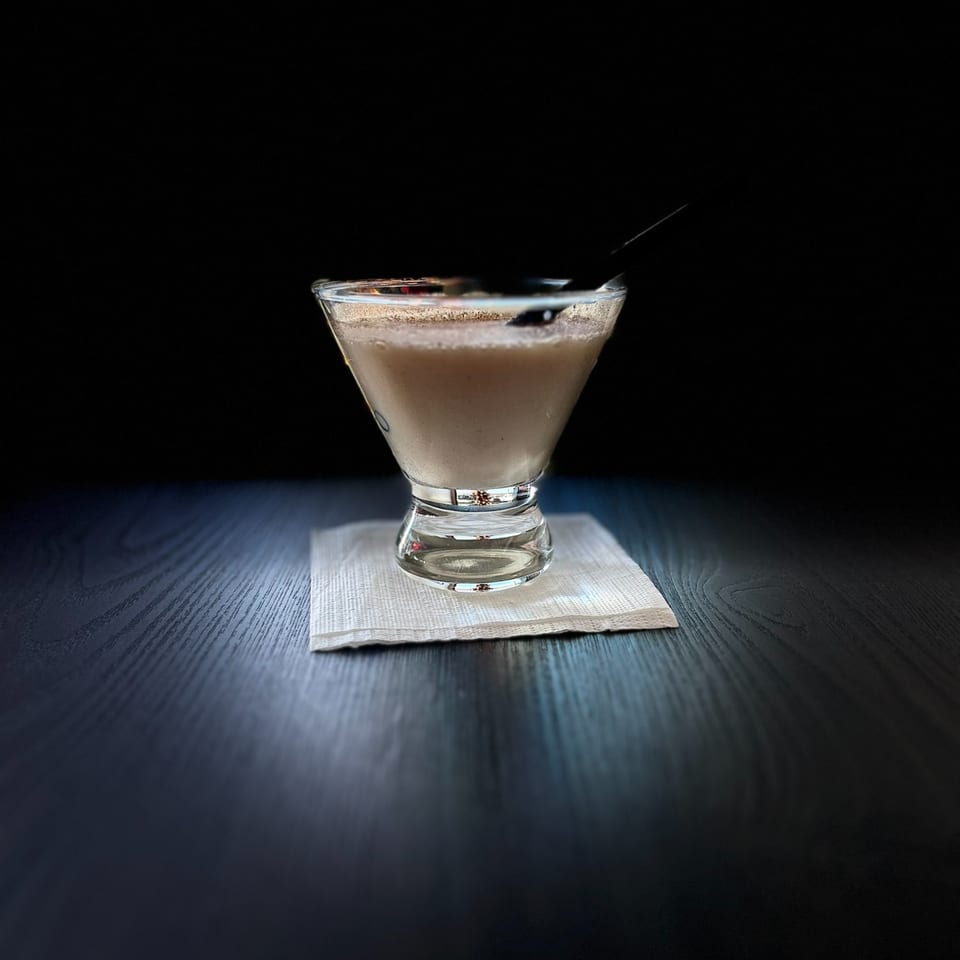 A creamy Moon Valley Grill & Patio cocktail in a martini glass with a dark straw on a napkin.