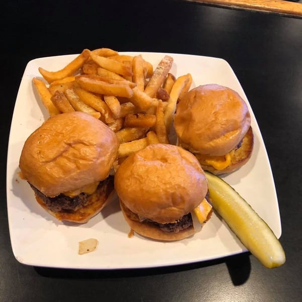 Three Moon Valley Grill cheeseburger sliders with fries and a pickle spear on a white plate.