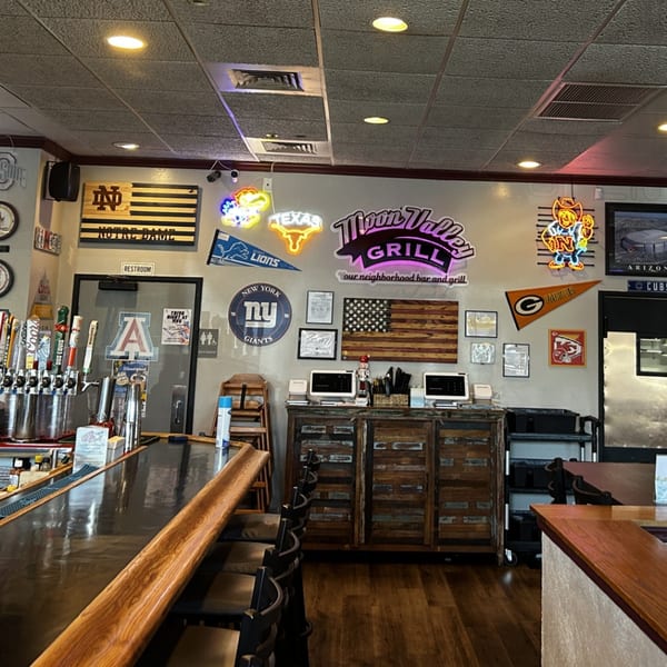 Interior of Moon Valley Grill & Patio bar area, featuring sports memorabilia, neon signs, and a wooden bar.